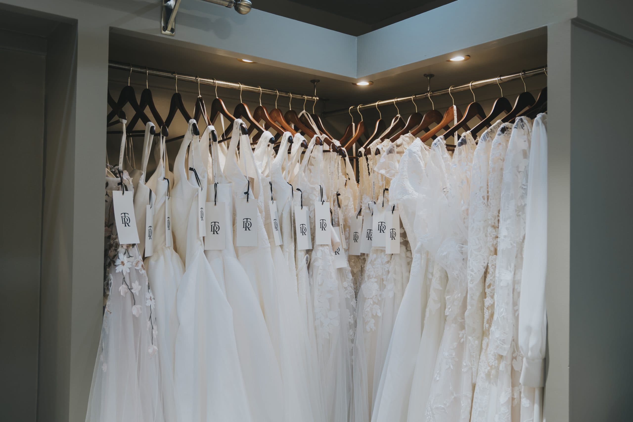Wedding dresses hanging in bridal boutique showroom with lace, satin, and designer gowns on display