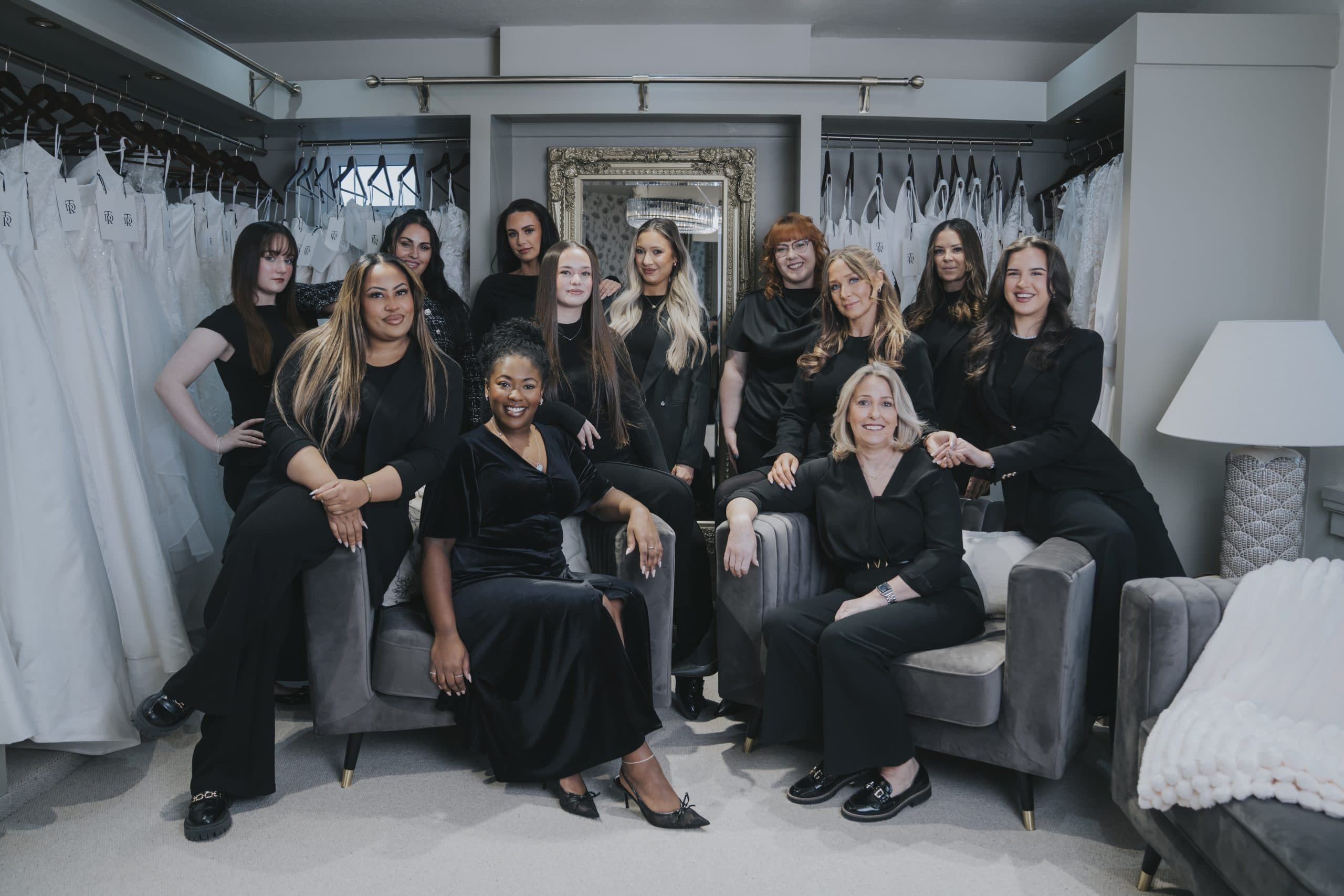 Bridal boutique stylists team group portrait surrounded by luxury wedding dresses in elegant showroom